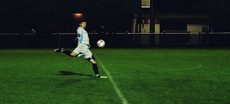 A man kicking a ball on a football field during football coaching in UAE.