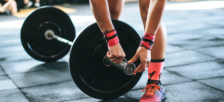 A person about to lift heavy adjusting the weight with the help of personal fitness trainer ajman