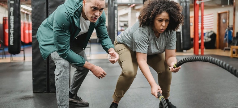 A woman exercising with battle ropes near a male coach showring how to choose a weight loss trainer in Abu Dhabi.