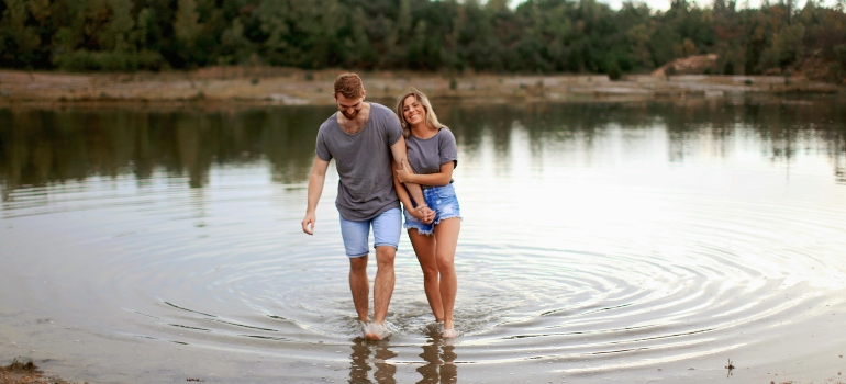 A couple wearing grey T-shirts walking on shallow water and talking about healthy date ideas in Sharjah.
