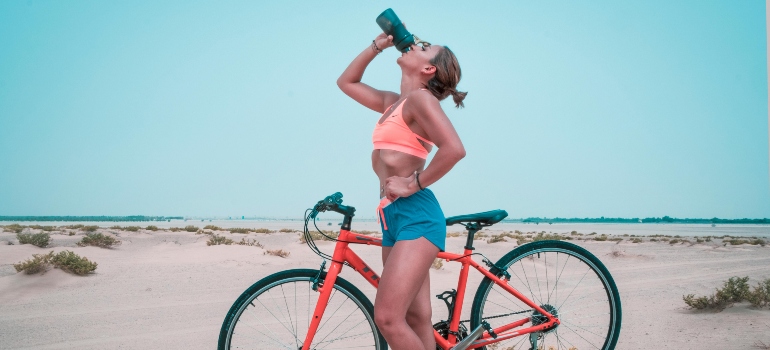 A woman is drinking water while thinking about ways to improve endurance for running in Dubai's climate.