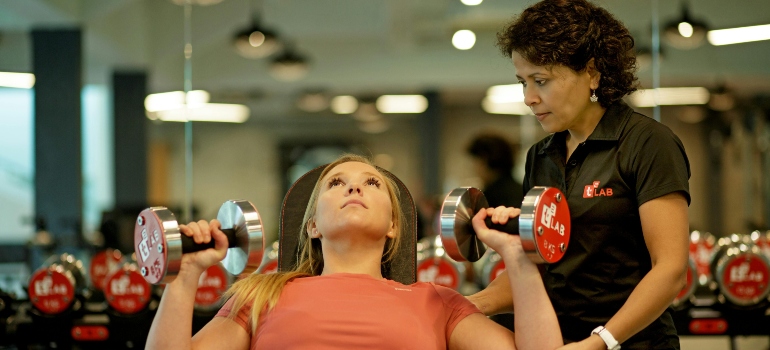 A girl with a personal trainer exercises in the gym.