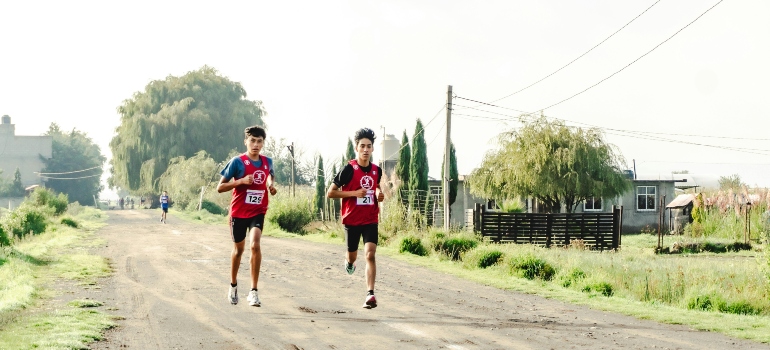 Two teenage boys in race bibs running on a dirt road in a countryside marathon.