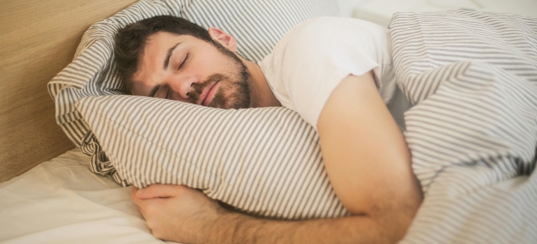 Person sleeping peacefully in bed, highlighting improved sleep quality as one of the key reasons to start working out as soon as possible.