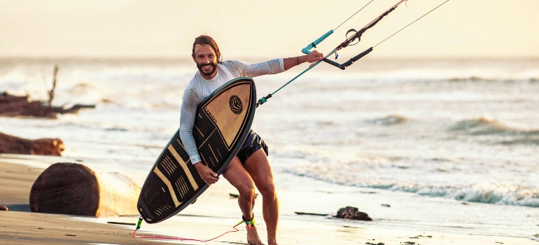 A man on the beach holding a kite surfing board.