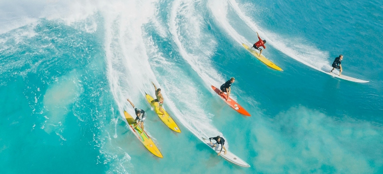 Group of surfers riding a giant wave together — Choose the Right Water Sport for Your Fitness Level in Dubai.