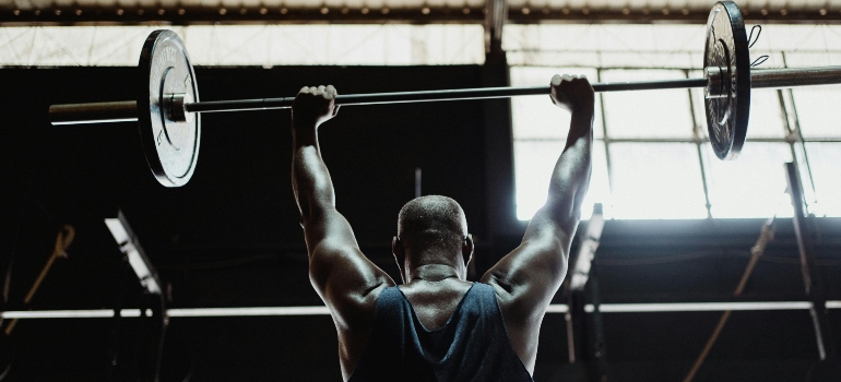 Athlete lifting a barbell overhead showcasing strength and progress using Muscle Gain Methods from Dubai’s Top Fitness Trainers.