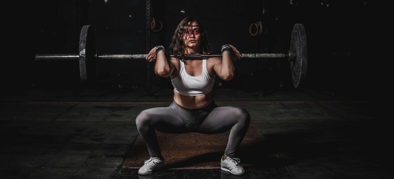 Woman lifting barbell in a squat position during intense strength workout at the gym.
