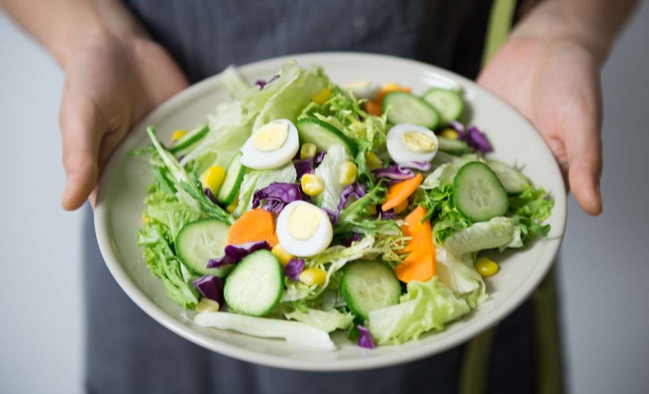 A person holding a plate with fresh veggies and boiled eggs